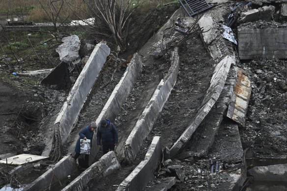 A couple walk across the Bakhmutovka River crossing where the bridge has been destroyed.