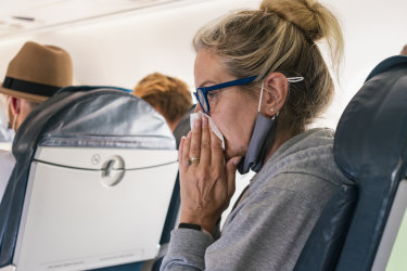 Woman sitting on a plane blowing her nose. 