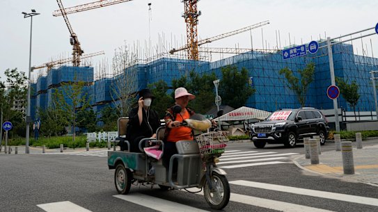 Residents on a tricycle ride past a car with a sign that reads “Country Garden homeowners rights protections car”, parked near homeowners camping outside the Country Garden One World City project on the outskirts of Beijing.
