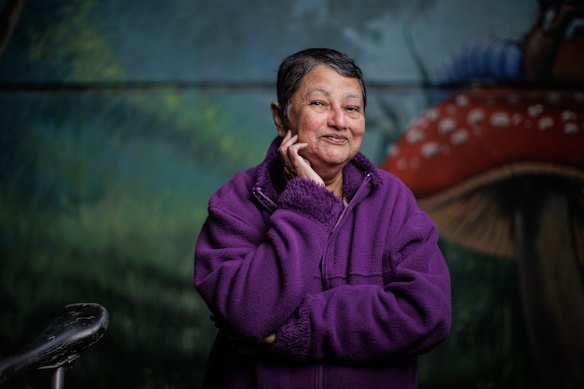 Mithrani/Mithra De Abrew Mahadeva, who identifies as non-binary and lives with mixed dementia, in front of an Alice in Wonderland mural at Frankston Library, which brings back happy childhood memories.