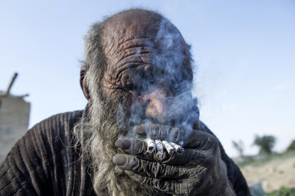 Amou Haji (Uncle Haji) smokes several cigarettes as he sits on the ground on the outskirts of the village of Dezhgah in the Dehram district of the south-western Iranian Fars province in 2018.