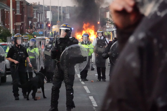 Riot police hold back protesters near a burning police vehicle after disorder broke out in Southport, England.