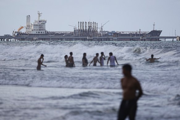 People in the surf near Puerto Cabello, Venezuela, as an oil tanker is seen anchored at the dock near El Palito refinery.
