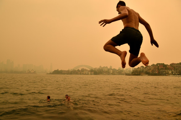 A swimmer dives into the harbour on Thursday while a smoky haze remains over Sydney. 