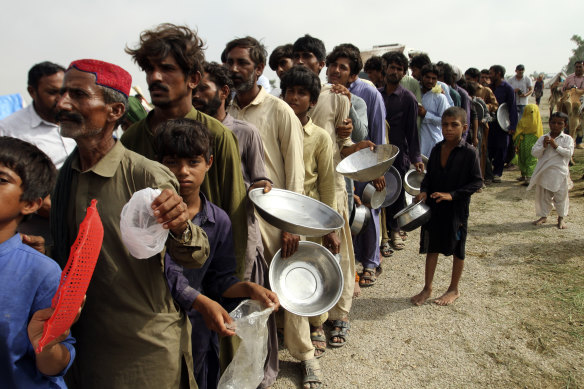 Flood-affected people queue with utensils to get food, distributed by Pakistani troops in Rajanpur.