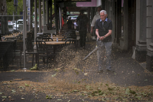 University Cafe owner Giancarlo Capriol cleaning up his shop front on Lygon Street after the storm. 