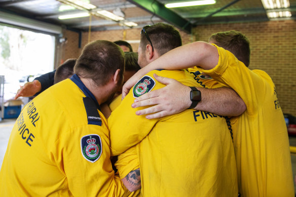 Members of the Horsley Park Rural Fire Brigade embrace while remembering their fallen comrades on Sunday. 