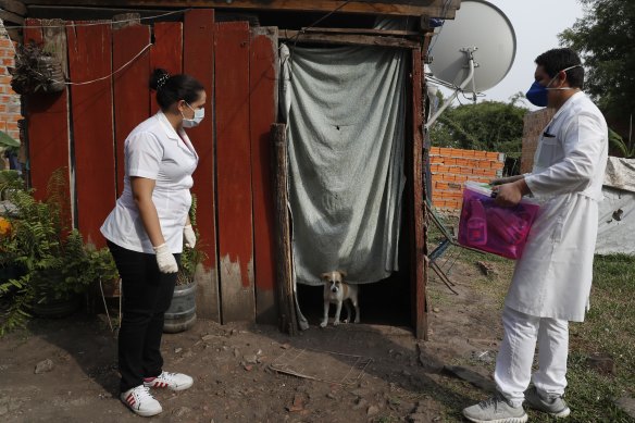 Two health workers wait for the occupant of a shack to come out to be tested for COVID-19 in Limpio, Paraguay.