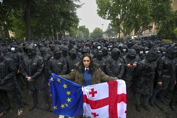A woman holds a Georgian national and an EU flags in front of riot police blocking a street to prevent demonstrators during an opposition protest against “the Russian law” near the Parliament building in the centre of Tbilisi, Georgia.