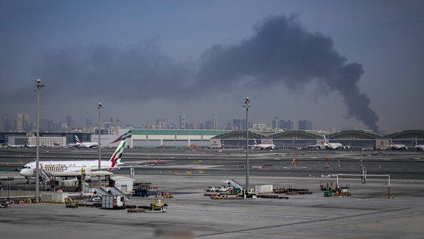 A plume of smoke caused by an Iranian strike is seen in the background as Emirates planes are parked at Dubai International Airport on Sunday.