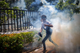 Kolombo'daki sokak şiddeti sırasında askerlerin göz yaşartıcı gaz kullanmasından sonra bir protestocu saklanmak için koşuyor.