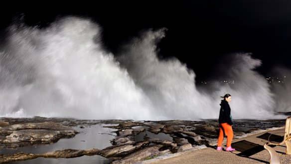 A person walks past large breaking waves at Clovelly beach on Saturday morning. 