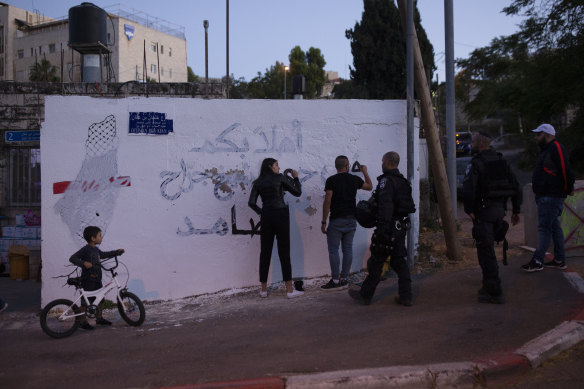 Palestinian activists are approached by Israeli police as they repair a mural defaced by an Israeli settler.  The male activist  was arrested after repainting the Arabic phrase “welcome to the steadfast neighbourhood of Sheikh Jarrah”.