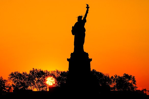 The sun rises behind the Statue of Liberty in New York City.