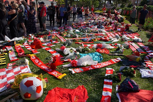 Football fans stand next to tributes in memory of Liverpool player Diogo Jota at Anfield Stadium.
