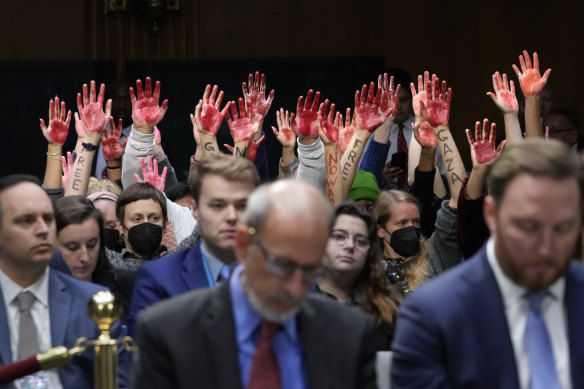 Anti-war activists raise their hands in protest as Secretary of State Antony Blinken calls for military aid to Israel.