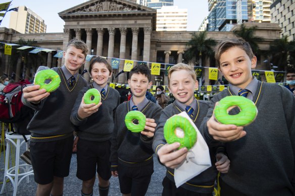 Year 6 boys from Marist College Ashgrove in King George Square   pose with green and gold donuts to celebrate that the city will host the 2032 Olympic Games. 
