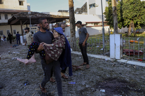 A Palestinian man carries an elderly woman past the site of the explosion at al-Ahli hospital. The Hamas-run Health Ministry says an Israeli airstrike caused the explosion that killed hundreds at al-Ahli, but the Israeli military says it was a misfired Palestinian rocket. 