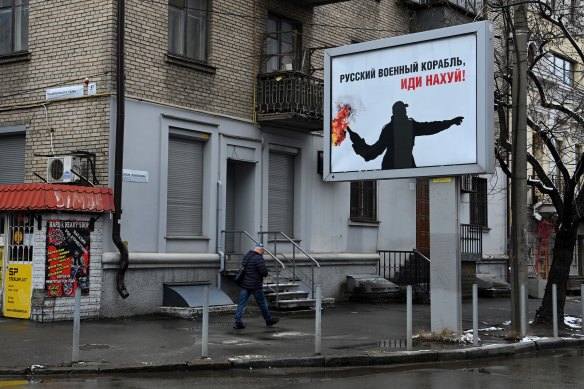 A man walks past a billboard that says “Russian military ship! Go f--- yourself” on the streets of Dnipro.