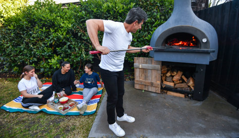 Chef Gianluca Bocci tends to his beloved wood-fire pizza oven as his wife Sandra and their daughters Chloe (13) Astrid (11) laugh nearby.