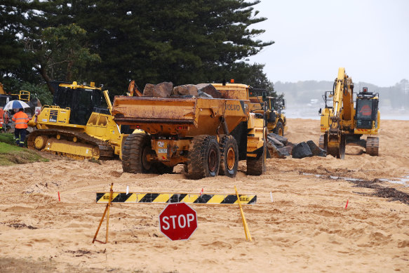 Earthmoving equipment moves boulders to create a sea wall to protect damaged houses at Wamberal on Sunday.