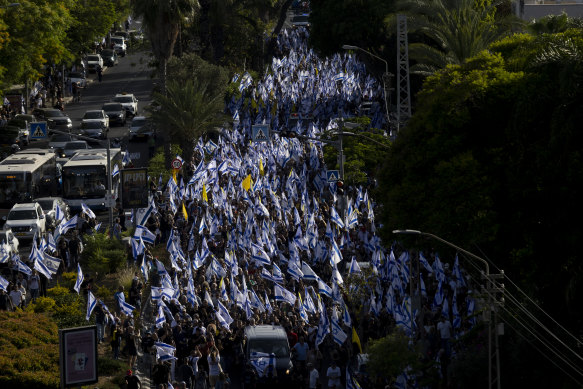 In Tel Aviv, people hold flags as they walk behind an ambulance carrying the body of Hanan Yablonka, who was taken hostage by Hamas on October 7. His body, along with two others, was recovered from north Gaza by IDF soldiers.