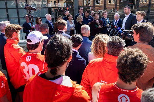 Swans players watch on as captain Callum Mills and coach Dean Cox talk to the media.