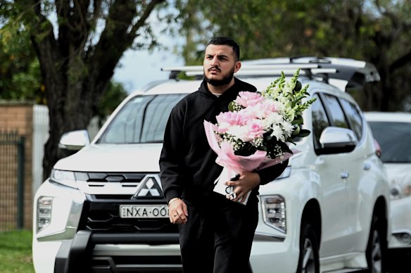 A man carrying flowers approaches the home where family and friends of John Versace have gathered.