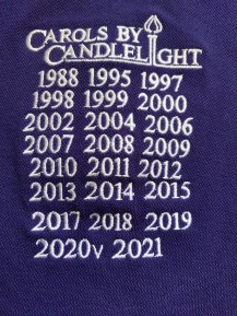 List on chorister Fiona Waters’ polo shirt of her years of singing at <i>Carols By Candlelight</i>. She performed last year virtually, so there’s a “v” after 2020.