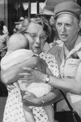A Red Cross nurse helps a woman with a baby away from the emergency buses.