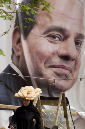A woman carries a tray of bread in front of an election poster for Egyptian President Abdel Fattah el-Sisi, in Cairo.