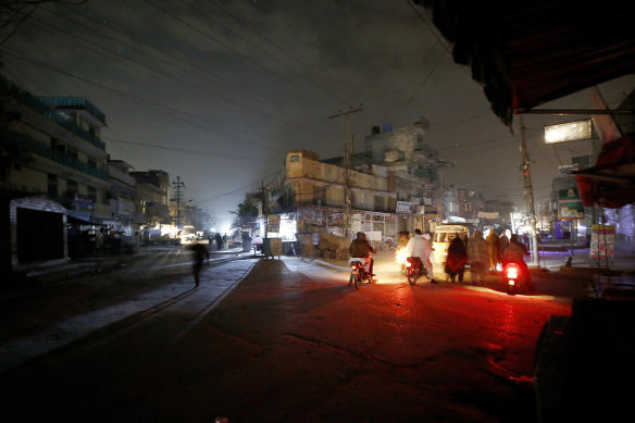 People are silhouetted on vehicles headlights on a dark street during widespread power outages in Rawalpindi, Pakistan, on Sunday, January 10.