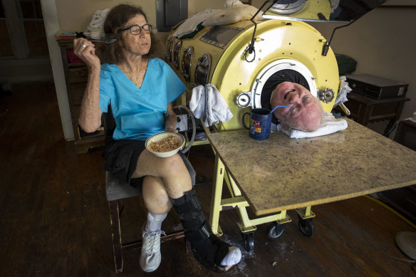 Attorney Paul Alexander chats with caregiver and friend Kathryn Gaines as he drinks coffee and she eats breakfast beside his iron lung at his home in Dallas. 