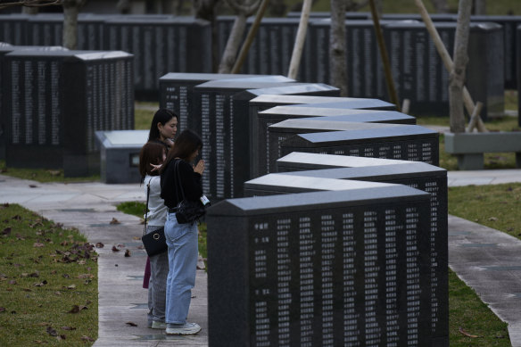 Kanai from Yokohama (only her last name provided), back, and her friends pray in front of a Cornerstone of Peace monument with the name of her grandfather imprinted, created in memory of those who died in Okinawa, at the Peace Memorial Park in Itoman.
