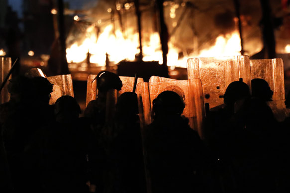Riot police watch the flames rise from a tent city set up by protesters. The tents were set on fire by men who appeared to be civilians, however they were accused of being members of a private unit of the parliamentary guards.