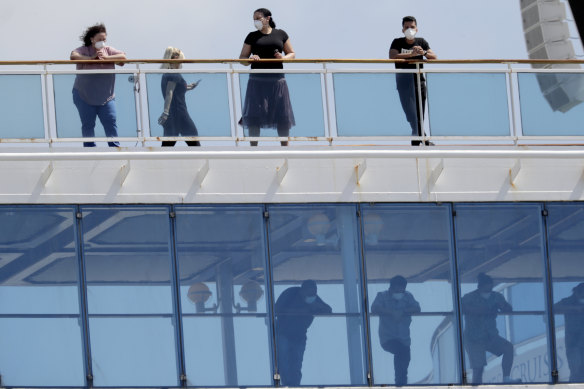 People wearing protective masks look out from the Coral Princess cruise ship while docked at Port Miami on Saturday.