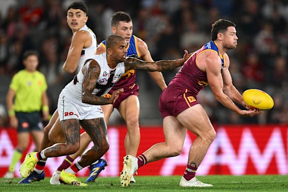 Lachie Neale of the Lions handballs whilst being tackled by Bradley Hill of the Saints.