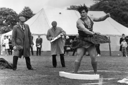 Judges check his footwork as Douglas Edmunds of Glasgow University wearing a kilt puts the shot, 1969.  