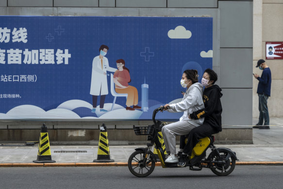 Women ride a scooter past a billboard for a COVID-19 vaccination drive.