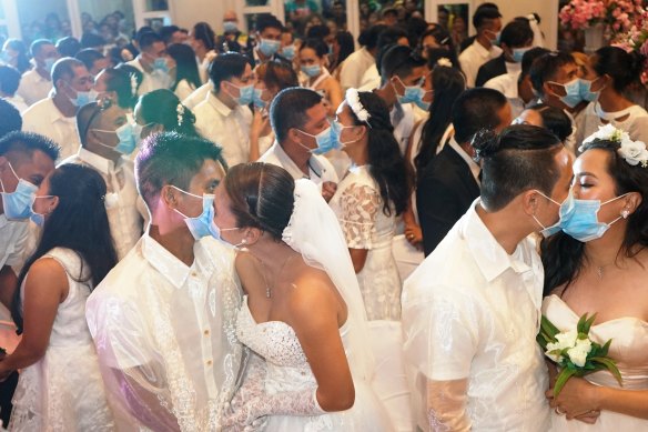 Filipino couples kiss each other while wearing masks provided by the City Health Office in an annnual mass wedding.