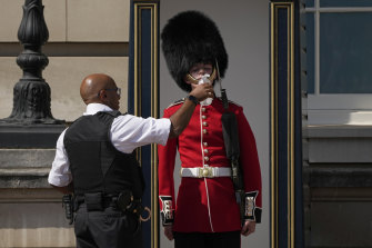 Bir polis memuru, Buckingham Sarayı'nın önünde nöbet tutan bir İngiliz askerine su veriyor.
