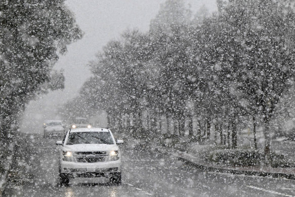 A vehicle makes its way across Wilson Avenue in Rancho Cucamonga, California, as snow begins to blanket the area at approximately the 1500-foot level on Saturday.