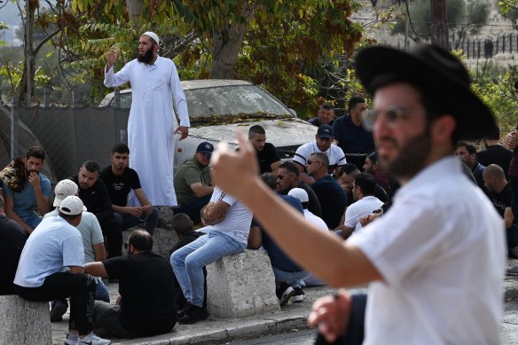 In the foreground, an Orthodox Jewish man gestures to other men as Muslim worshippers pray outside the Al Aqsa Mosque after having been refused entry.