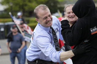 Initiative promoter and gubernatorial candidate Tim Eyman disregards social distancing guidelines as he leans in to place a sticker on a child's back at a protest opposing Washington state's stay-home order on Sunday.