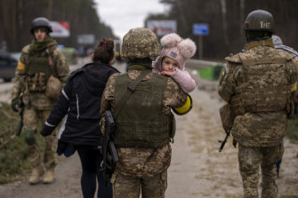 A Ukrainian soldier carries a child, helping a fleeing family to cross the Irpin river on the outskirts of Kyiv.