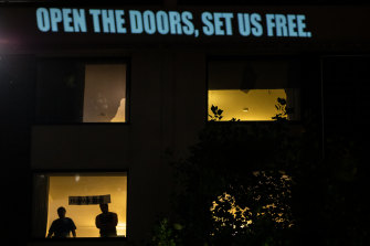 Refugees stand behind tinted windows at an immigration detention hotel in Melbourne.