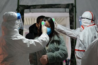 Government workers take the temperature of passengers as they exit a railway station in Fuyang in central China's Anhui Province.