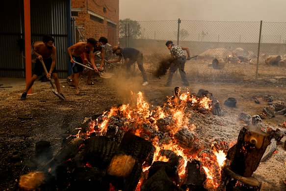 Young people try to extinguish a fire outside a house as wildfires surround a Spanish village.