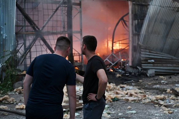 Men stand near a fire after a jet-powered drone struck an office building in the Podilskyi district of Kyiv on Friday (Ukrainian time).