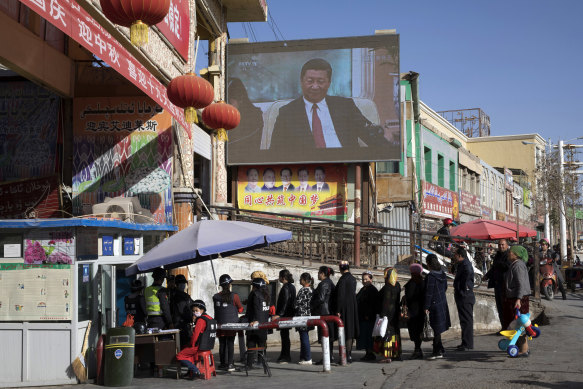 Residents line up at a security checkpoint into the Hotan Bazaar where a screen shows Chinese President Xi Jinping in Hotan in western China’s Xinjiang region.